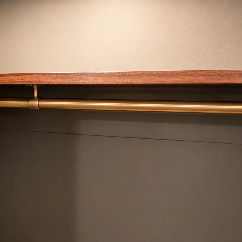 Closet with wooden shelf and gold rod against a neutral wall.