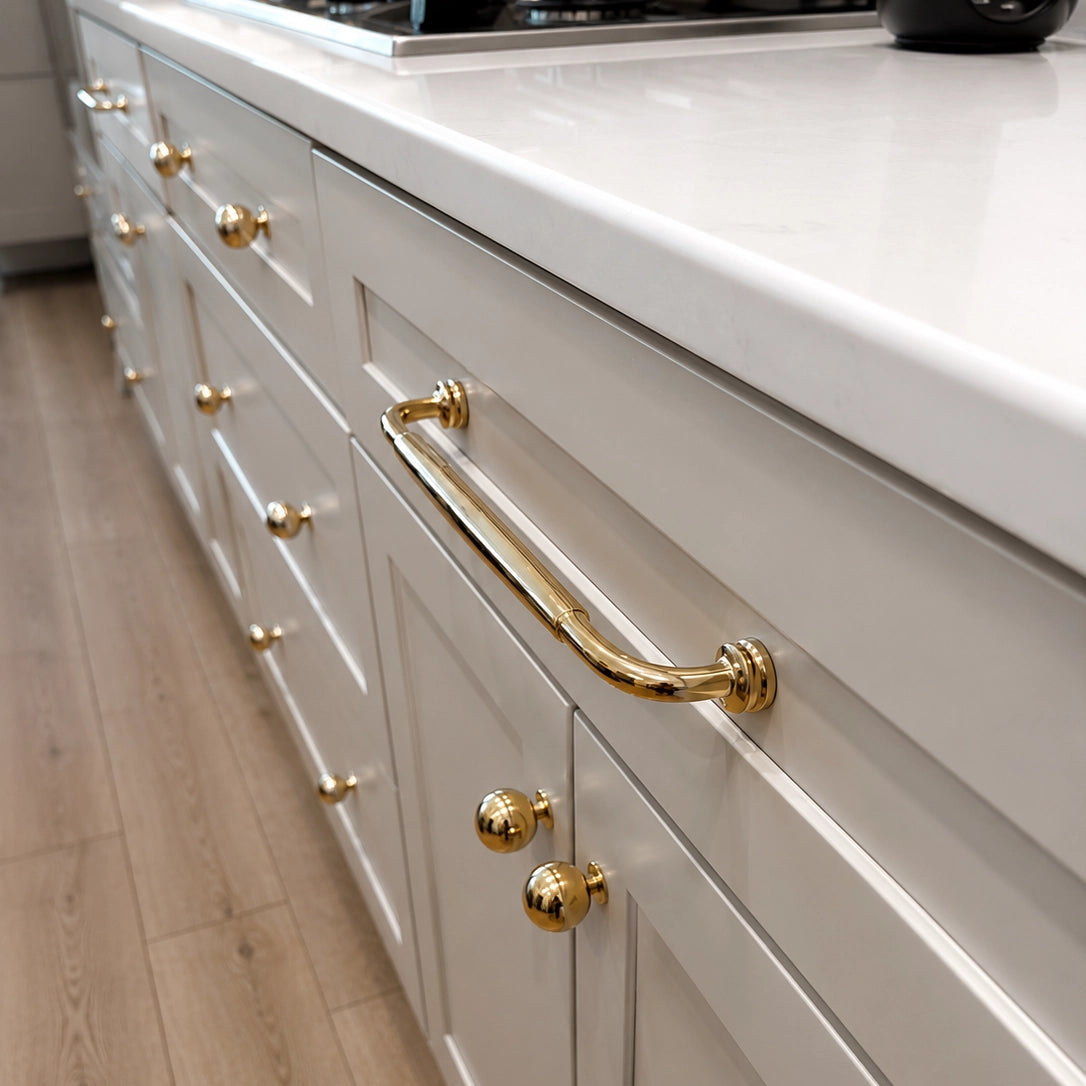White kitchen cabinets with gold handles and knobs on a wooden floor.