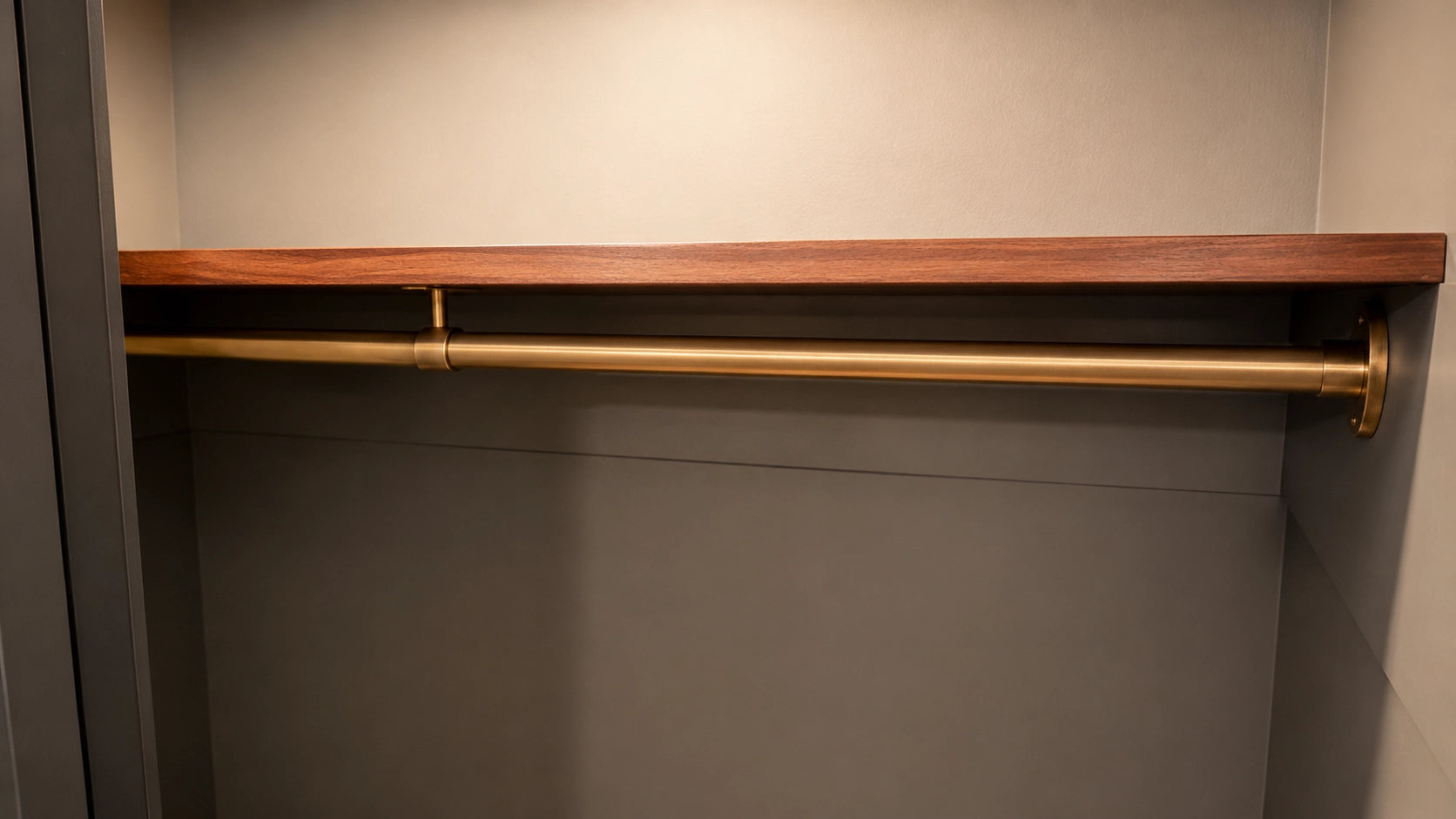 Closet with wooden shelf and gold rod against a neutral wall.