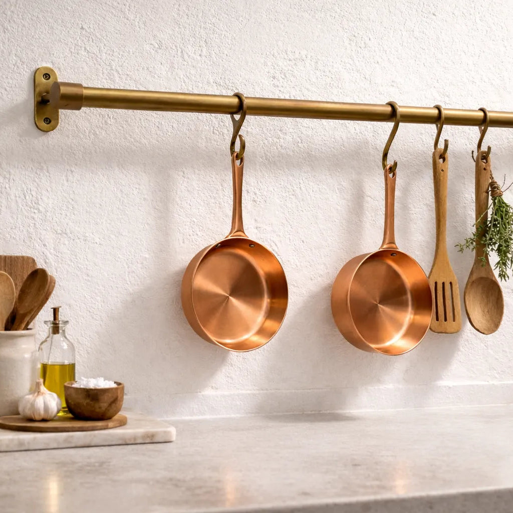 Copper pots and pans hanging on a brass rod in a kitchen setting.