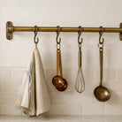 Kitchen utensils hanging on a brass rod against a white tiled wall.