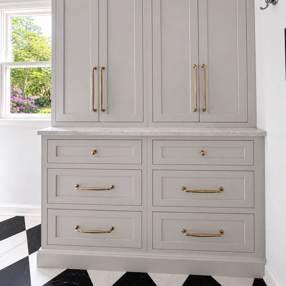 Gray cabinet with gold handles in a room with a window and black and white checkered floor.